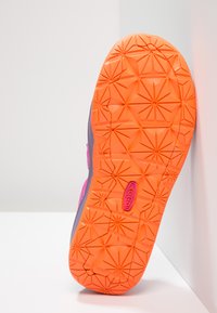 Skoled med et geometrisk mønster i oransje og grått, med en ikke-merkerende tekstur og en fremtredende logo i rosa.