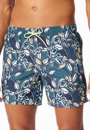 Male torso and upper legs wearing blue swim shorts with a light floral pattern and a light yellow drawstring tied at the waist.