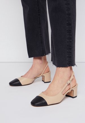 Beżowe buty typu slingback wykonane ze skóry z czarnym zaokrąglonym noskiem. Posiadają grube obcasy i regulowany pasek z klamrą. Gładka faktura.
