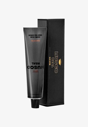 Schwarze Tube mit Musgo Real Rasiercreme mit matter Oberfläche, mit geprägtem Text und einem klassischen Logo, aufrecht neben einer schwarzen Box platziert.