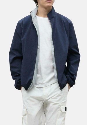 Chaqueta navy con forro gris, cierre frontal con cremallera y puños acanalados. Fabricada en una tela suave y ligera; presenta un diseño minimalista.
