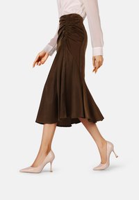 Gonna in raso marrone con design svasato, dettagli arricciati in vita, abbinata a décolleté rosa pallido con punta affusolata.