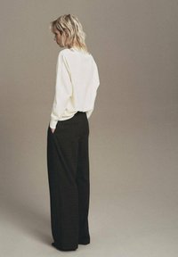 Pantalones negros de pierna ancha combinados con un suéter crema de corte holgado. El suéter tiene una silueta relajada y detalles sutiles en la parte posterior.