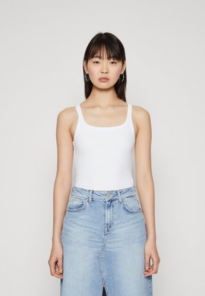 Hvid ribbet tanktop med brede stropper, parret med en lyseblå denimnederdel med en frontslids og traditionelt fem-lomme design.