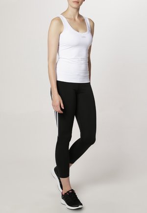 Bílý bezrukávový top v kombinaci s černými legínami se bílými pruhy. Oblečení je vyrobeno z elastických, prodyšných materiálů.