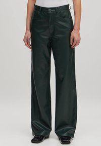 Groene faux leren broek met wijde pijpen en een zachte textuur, twee voorzakken en een standaard tailleband. Gedetailleerde stiksels zichtbaar.