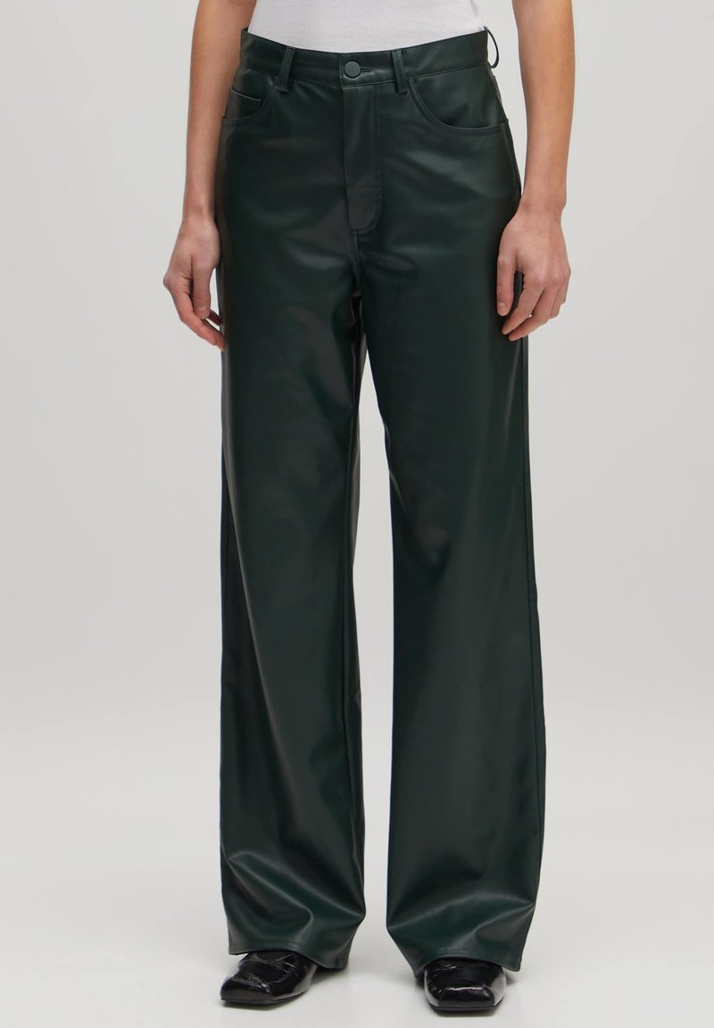 Groene faux leren broek met wijde pijpen en een zachte textuur, twee voorzakken en een standaard tailleband. Gedetailleerde stiksels zichtbaar.