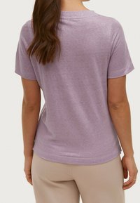 Svetle fialové tričko s krátkým rukávem, volnějšího střihu, měkkou texturou a zaobleným výstřihem, spárované s béžovými kalhotami.
