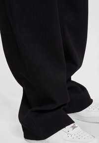 Black ribbed wide-leg pants with a textured surface, paired with white sneakers featuring perforated detailing and lace-up closure.