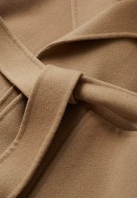Manteau en laine beige noué avec une large ceinture à la taille, montrant une texture douce et des détails de couture nets.