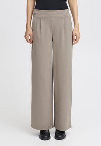 Svetlo rjave široke hlače z naborki in ravnim pasom, narejene iz mehkega, raztegljivega materiala; v kombinaciji s črnimi gležnjači.