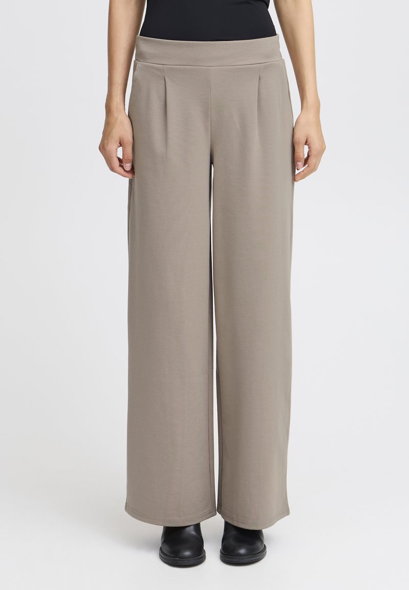 Svetlo rjave široke hlače z naborki in ravnim pasom, narejene iz mehkega, raztegljivega materiala; v kombinaciji s črnimi gležnjači.