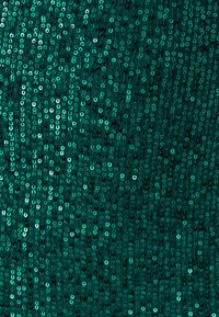 Blizgi žalia blizgančiais kalną primenanti medžiaga su tekstūruotu paviršiumi, kurioje tankiai išdėstyti maži apvalūs blizgučiai įvairių žalių atspalvių.