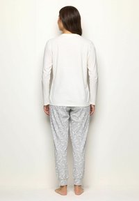 Maglietta bianca a maniche lunghe con scollatura tonda abbinata a pantaloni grigi chiari con vita elastica e un motivo circolare bianco.