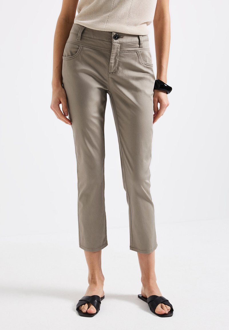 Pantalons cropped gris clair avec poches avant, passants de ceinture et fermeture à bouton, associés à des sandales noires à glissière, sur un fond uni.