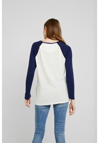 Witte en marineblauwe lange mouwen raglan T-shirt, zachte textuur, ronde zoom, mouwen in contrastkleur, casual pasvorm, met minimale branding.