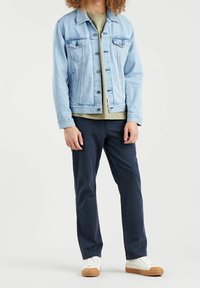 Lekka kurtka jeansowa o klasycznym kroju, z dwoma przednimi kieszeniami, zapięciem na guziki i wyblakłym wykończeniem, w zestawie z oliwkową zieloną koszulą i granatowymi spodniami.