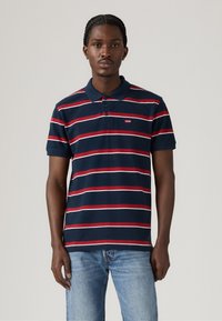 Πολυφορεμένο πουκάμισο polo με ναυτικές ρίγες σε κόκκινο και λευκό, τριών κουμπιών λαιμόκοψη και λογότυπο Levi's στο αριστερό στήθος. Μαλακό βαμβακερό ύφασμα.