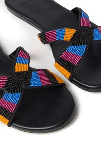 Sandalias planas negras con tiras cruzadas decoradas con cuentas en patrones azules, rosas, naranjas y negros. Textura suave con un diseño minimalista.