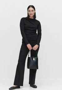 Svart långärmad topp och utsvängda byxor i kombination med en strukturerad svart handväska. Slät tyg, minimalistisk design och svarta platta skor.