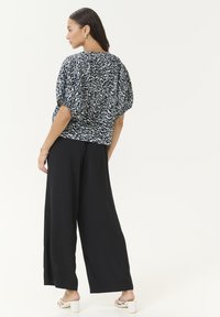 Haut texturé à motifs bleu marine et blanc avec des manches bouffantes, associé à un pantalon large noir et des sandales à talons blanches.