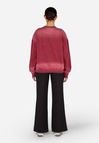 Burgundská mikina s voľným strihom, rebrovanými manžetami a lemom, v kombinácii s čiernymi širokými nohavicami a bielymi teniskami. Hladká textura.