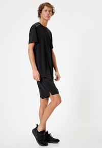 Sort atletisk t-shirt med korte ærmer, kombineret med sorte shorts og sorte sneakers. Glat stof med en afslappet pasform og sideslids.