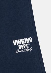 Tamno plave pamučne trenirke s bijelim logotipom na kojem piše "VINGINO DEPT. Denim Supply." Tekst je smješten s lijeve strane.