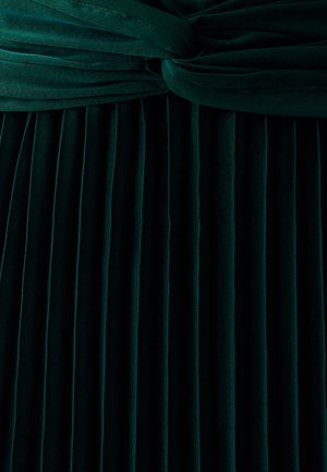 Tamsiai žalia plisėta suknelė, pagaminta iš minkštos aksomo medžiagos, su mazguota liemens detale ir vertikaliomis raukšlėmis visame sijone.