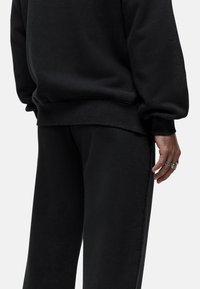 Schwarzes Sweatshirt mit lockerer Passform, gepufften Ärmeln und weicher Textur. Schwarze Sweatpants mit entspannter Silhouette und Seitennähten.