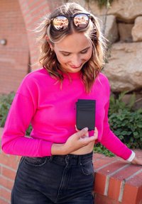 Black leather card holder featuring multiple slots and a zippered compartment, held in a hand; worn with a bright pink crop top and black jeans.