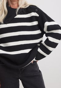 Sweter w czarno-białe paski o prążkowanej teksturze, z wysokim dekoltem, szczegółami guzika po bokach i luźnym krojem.