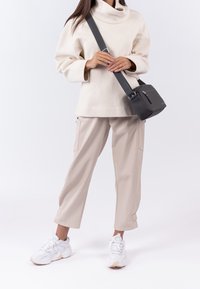 Maglione oversize crema, pantaloni cargo beige con tasche laterali, sneakers bianche e una piccola borsa a tracolla nera con dettagli zip.