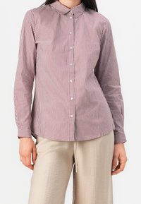 Pasiasta koszula na guziki w kolorze bordowym i białym, wykonana z bawełny, z klasycznym kołnierzykiem, długimi rękawami i zaokrąglonym dołem. W połączeniu z beżowymi spodniami.