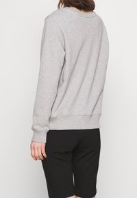 Maglione grigio con maniche lunghe, colletto alla americana e polsini a costine, abbinato a pantaloni corti neri. Tessuto misto cotone con una texture liscia.