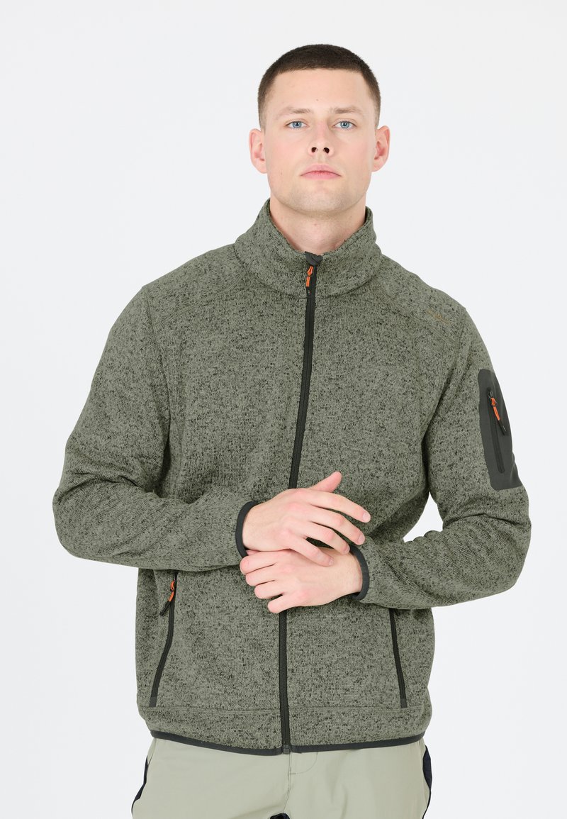Olijfgroene fleecejack met hoge kraag, een rits aan de voorkant, zwarte accenten en zijzakken. Heeft een mouwzak met een oranje rits.
