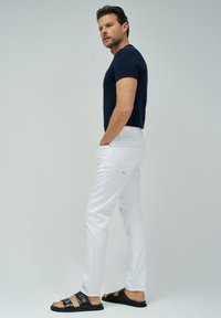 Pantalones ajustados blancos, camiseta ajustada azul marino y sandalias negras. Tela suave con un diseño minimalista; los pantalones cuentan con bolsillos traseros y un sutil logotipo.
