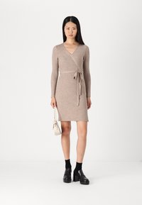 Robe en tricot beige à côtes, à manches longues, avec une taille ceinturée et une silhouette ajustée. Associée à des chaussures à plateforme noires et un petit sac blanc.
