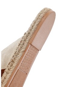 Suela de zapato espadrille beige con ribete de yute trenzado y secciones de goma texturizada para agarre, inclinada para mostrar el patrón de la suela y el detalle de las costuras.