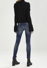 Jeans ajustados en denim azul oscuro, con un corte clásico y un ligero desvanecimiento. Combinados con una blusa de punto negra y botas de tobillo con un tacón grueso.