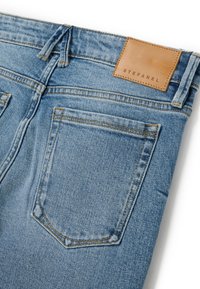 Hellblaue Jeans aus Denim mit einem Lederpatch, das "STEFANEL" beschriftet ist, standardmäßigen Gesäßtaschen mit Nähdetails und einem klassischen Schnitt.