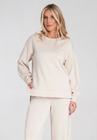 Beżowy sweatshirt o luźnym kroju, okrągłym dekolcie, obniżonych ramionach i ściągaczach. Połączony z dopasowanymi spodniami z tego samego materiału.