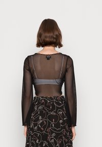 Czarna, przezroczysta bluzka z długim rękawem i falbankowym dekoltem, nałożona na szary stanik. W zestawie spódnica z kolorowym abstrakcyjnym wzorem twarzy.