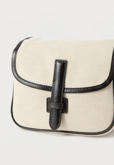 Μπεζ υφασμάτινη τσάντα με υφή, με λεπτομέρειες από σκουρό καφέ δέρμα και κούμπωμα με λουράκι στη μπροστινή πτυχή, εμφανιζόμενη σε λευκό φόντο.