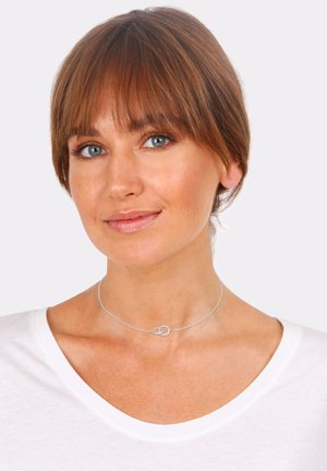 Silver choker necklace featuring two interlinked circles, fine chain design, worn by a woman with a natural makeup look and short hair.