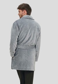 Bata de baño de corduroy gris con cuello chal, cintura con cinturón y tela texturizada, vista desde la parte posterior. Cuenta con mangas largas y bolsillos laterales.