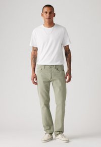 Hellgrüne Jeans mit geradem Bein, kombiniert mit einem schlichten weißen T-Shirt und weißen Sneakers. Merkmale sind sichtbare Nähte und ein einfaches Design.
