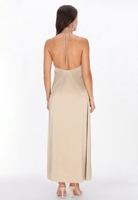 Beige maxi-jurk met halternek en een rugloze design. Gladde, zijden stof; voorzien van strikjes bij de nek en een hoge split tot boven de dij.