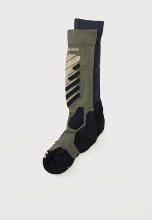 Deux paires de chaussettes montant jusqu'aux genoux, une olive avec des motifs géométriques noirs et beiges, l'autre uni bleu marine foncé, posées à plat.