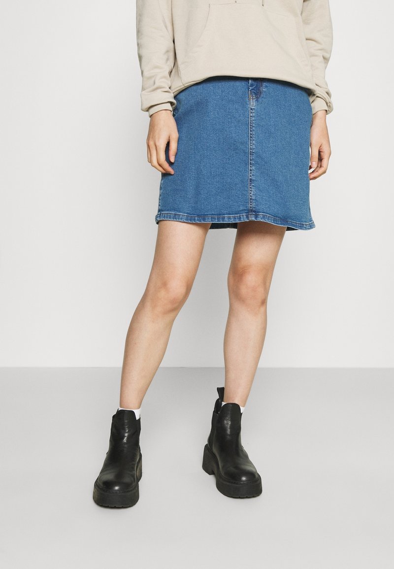 Džínová sukně v středně modré barvě se střihem do rovna a roztrhaným lemem. Kombinováno s černými kotníkovými botami a béžovou mikinou s kapucí.